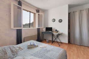 A bedroom with a bed, a desk with a computer, a window with curtains, and a door with a curtain.