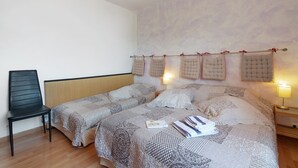 A bedroom with two beds, a chair, and a nightstand with a lamp.