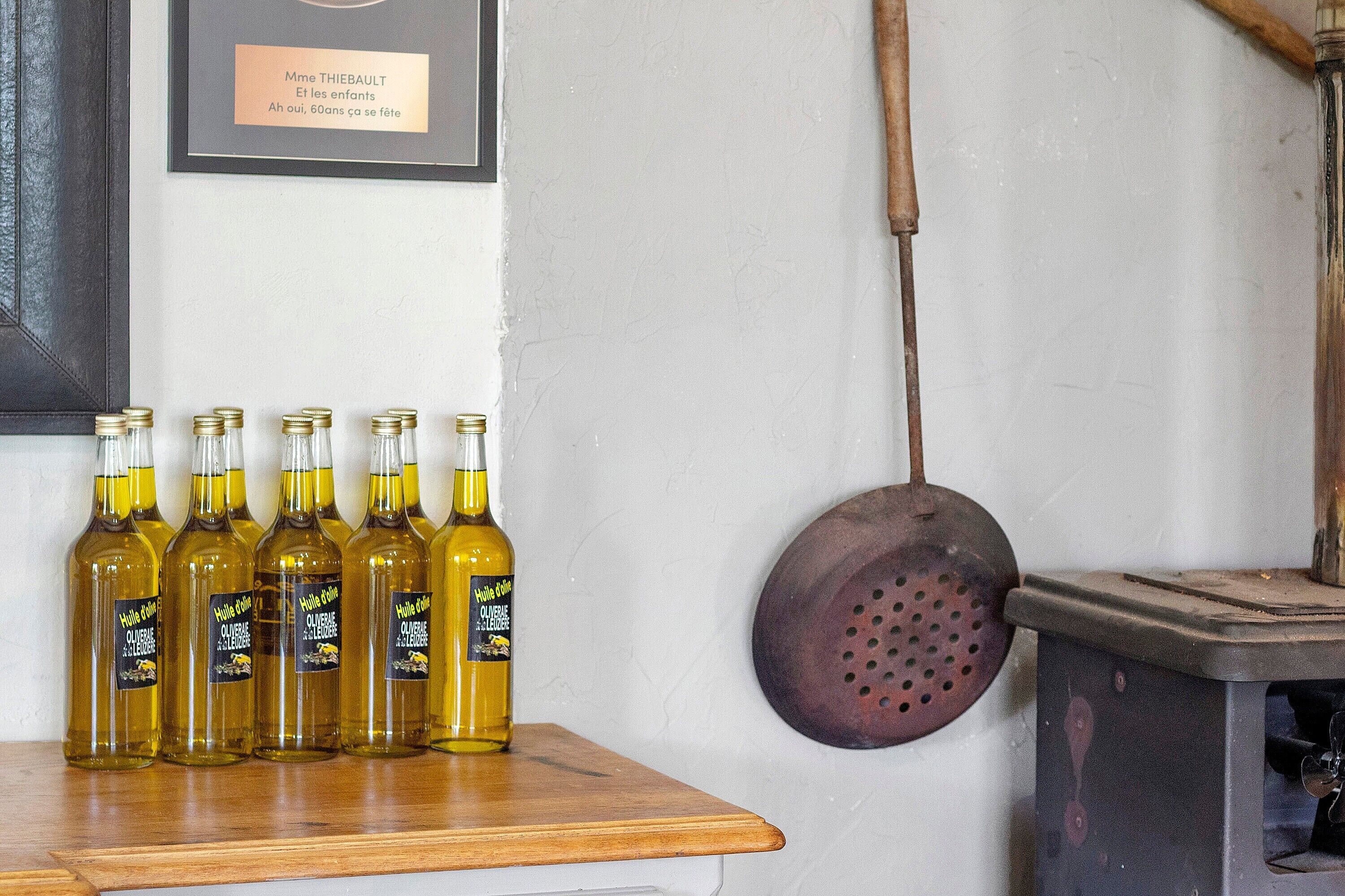 Un tavolo in legno con diverse bottiglie d'olio d'oliva, una targa a parete e un antico torchio per olive.