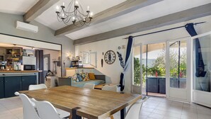 A dining area with a wooden table and white chairs, a kitchen in the background, and a sliding glass door leading to an outdoor area.