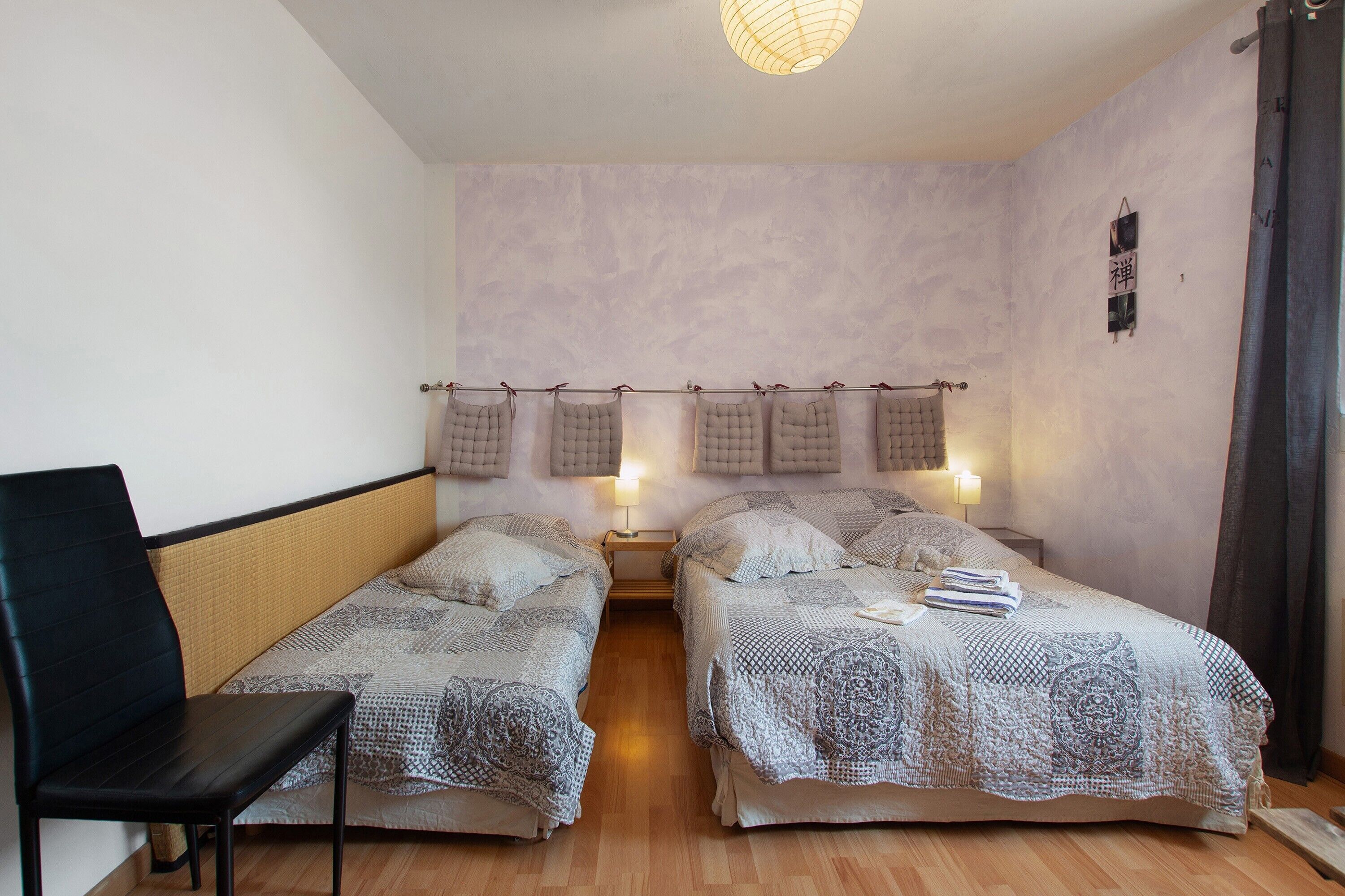 A room with two beds, a chair, and a hanging light fixture.