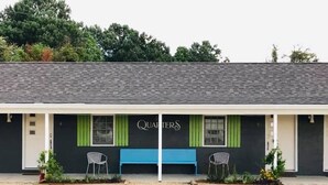 Un edificio de fachada negra, con contraventanas verdes y un banco azul en la entrada.