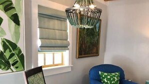 Una habitación con una silla de madera, un sofá azul, un tapete estampado, una araña y obras de arte en las paredes.