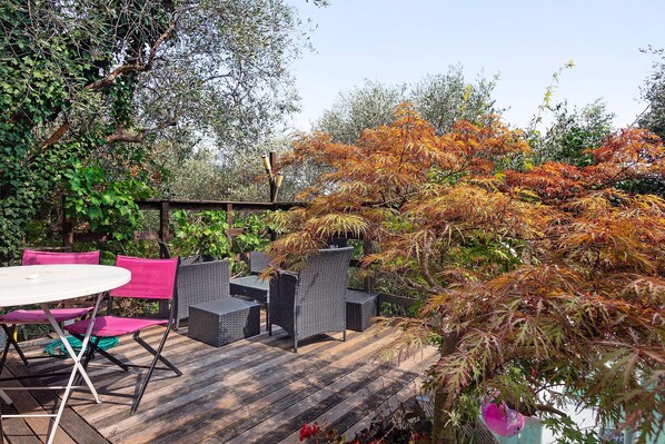 An outdoor patio with a round table and chairs, a pergola, and a variety of trees and plants.