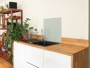 Eine Küche mit Holzausziehtisch, weißen Schränken, einer schwarzen Spüle und einer Pflanze links.