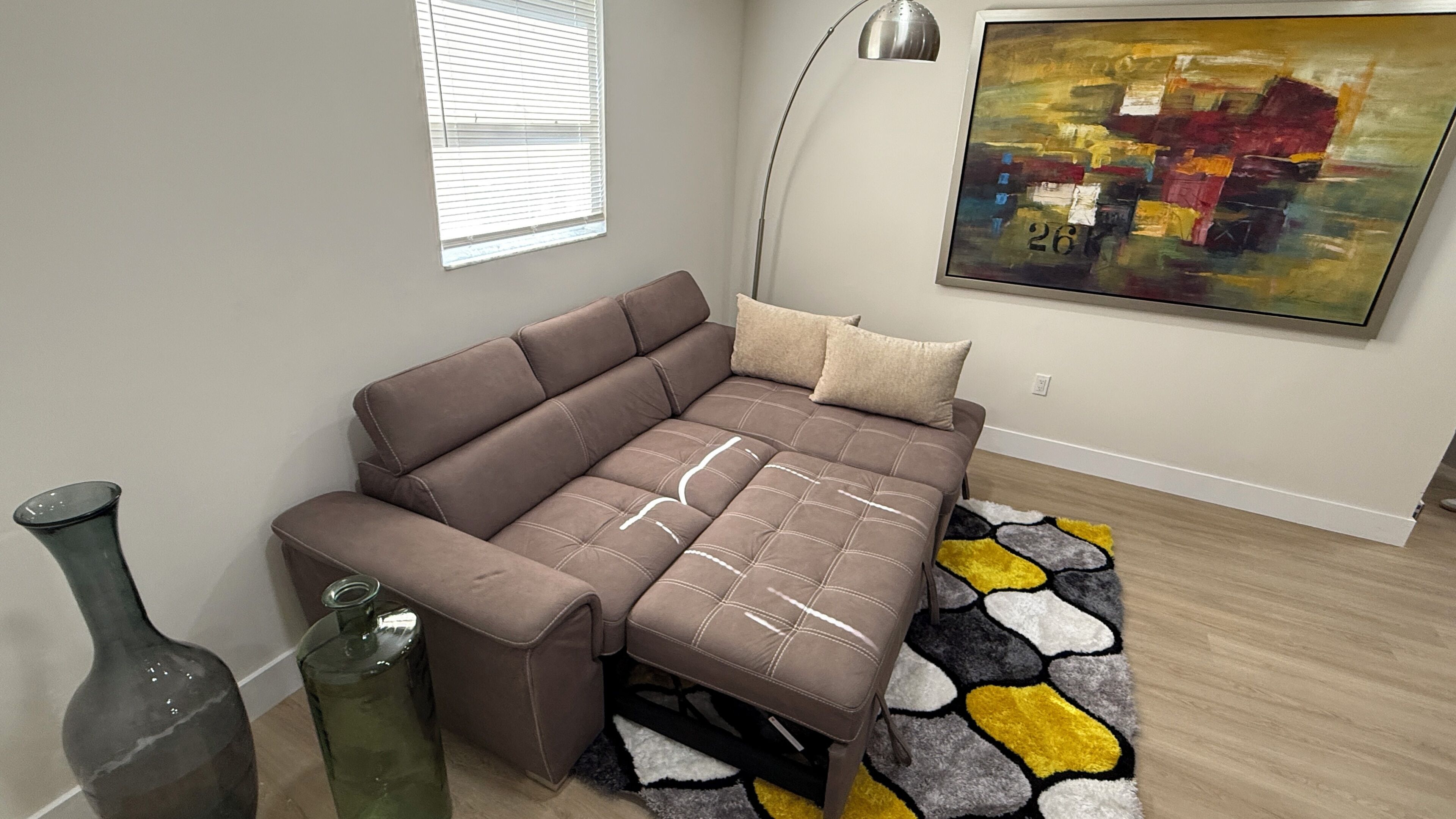 A modern living room with a sectional sofa, a floor lamp, a painting, and a patterned rug.