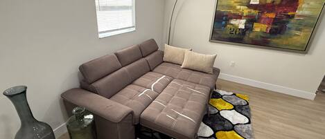 A modern living room with a sectional sofa, a floor lamp, a painting, and a patterned rug.