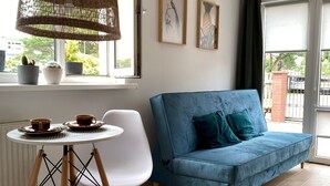 Een kamer met een blauwe bank, een witte stoel, een klein rond tafeltje met twee kopjes, en een hanglamp.