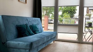 Een moderne woonkamer met een blauwe bank, een schuifdeur naar een buitenruimte en een betegelde vloer.