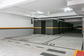 A parking garage with marked parking spaces, a car in the background, and a yellow stripe on the walls. - 350m from Beira-Mar | Pool | Gym #CA103 (Florianópolis)