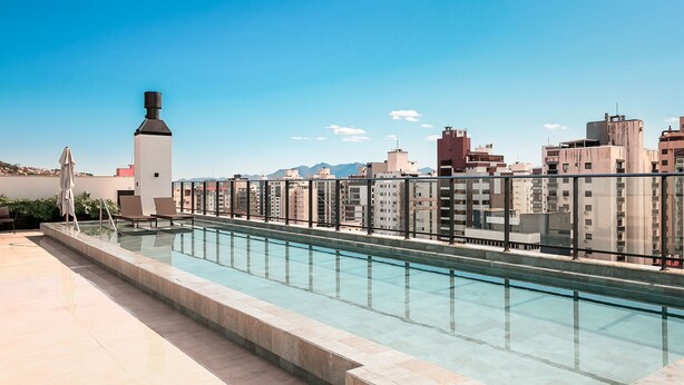 Una piscina en la azotea con barandilla de cristal, sillas de descanso y vistas a la ciudad.