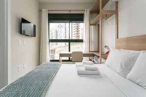 Habitación de hotel con cama, escritorio, silla, televisión y vistas a la ciudad.