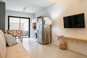 Un espacio habitable moderno con un sofá, una zona de comedor, lavadora, televisor y ventilador de techo.