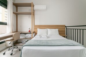Ein Hotelzimmer mit Bett, Schreibtisch, Stuhl, Ablagefläche mit Handtüchern und einem Fenster mit Vorhängen.