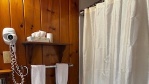 Et badeværelse med trævæg, et hvidt toilet, en hårtørrer på en hylde og et bruseforhæng.