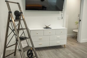 Ein Zimmer mit einem weißen Schrank, einem an der Wand montierten Fernseher und einer Metall-Leiter.