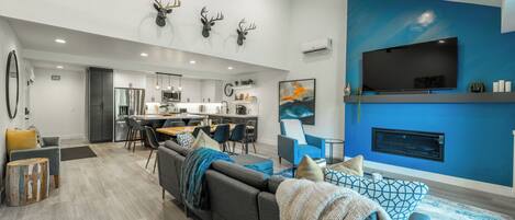 Una sala de estar moderna con un sofá gris, cojines azules decorativos, una chimenea y un televisor montado.