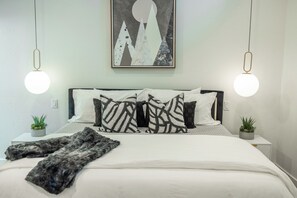 A neatly made bed with a patterned throw, two bedside tables with potted plants, and a wall-mounted abstract painting. - Modern Lower DV/Old Town + Hot tub and views (Park City)