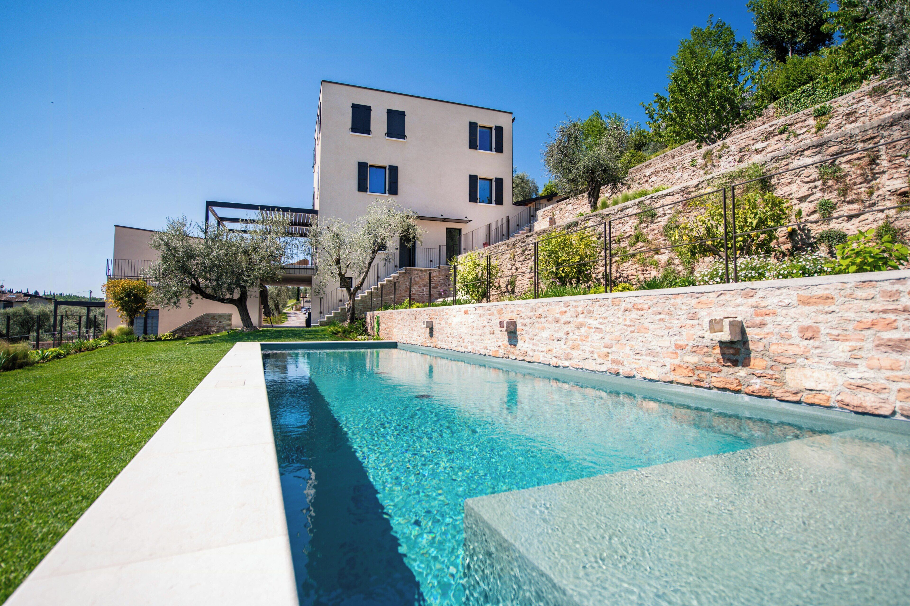 A modern house with a swimming pool, stone walls, and a clear blue sky.