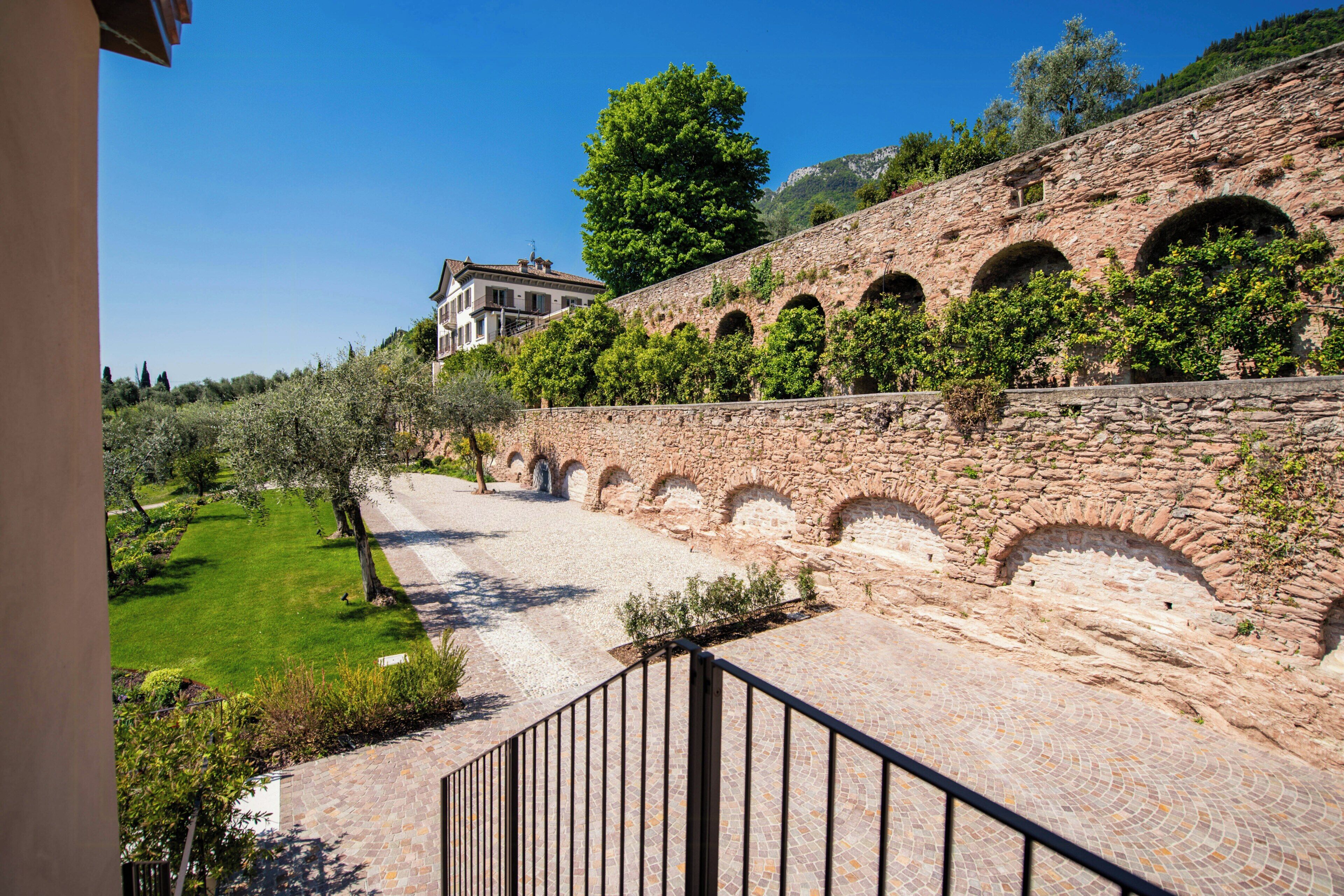 A stone wall with arches, a paved pathway, and a building in the background.