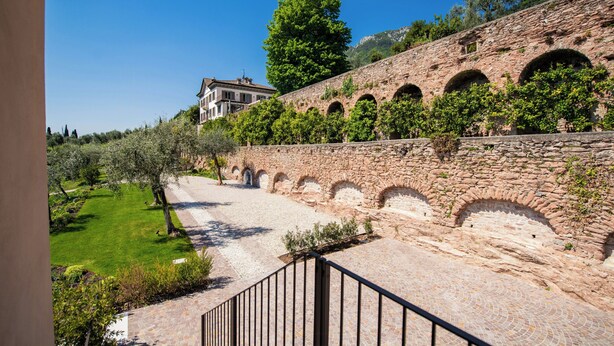 A stone wall with arches, a paved pathway, and a building in the background. - Torre with pool and lake-view terraces in Gargnano (Gargnano)