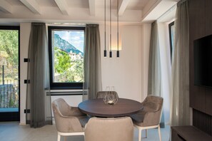 A modern dining area with a round table, four chairs, and a view of a mountainous landscape through a large window. - Torre with pool and lake-view terraces in Gargnano (Gargnano)