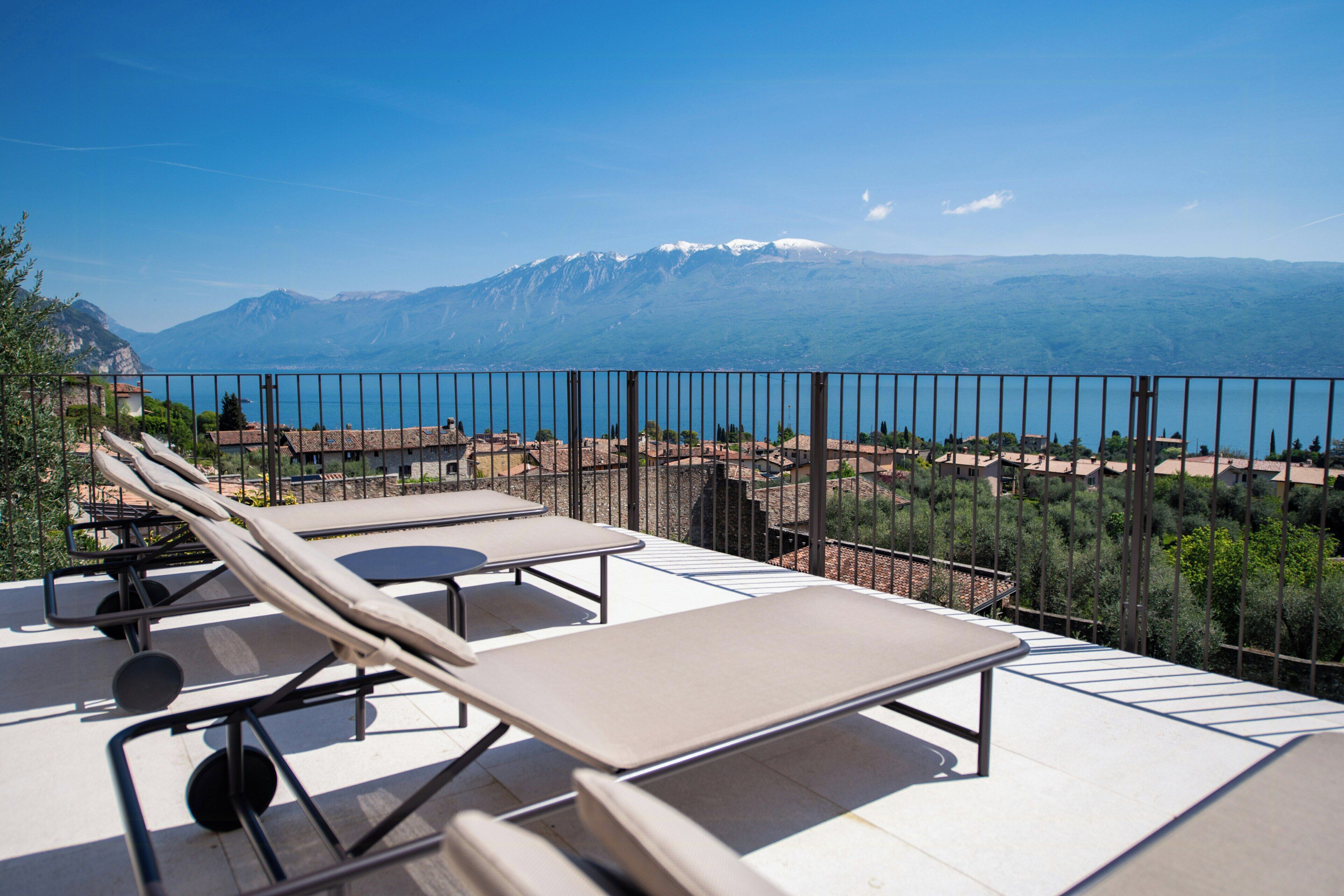 Una terraza con sillones de descanso y vistas a una cadena montañosa y un cuerpo de agua.