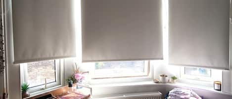 Una habitación con radiador, ventana con vistas, escritorio con cajones y maleta.