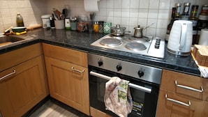 A kitchen with wooden cabinets, a gas stove, a microwave, and various kitchen utensils. - Cute studio apartment on café street close to music venues and camden (London)