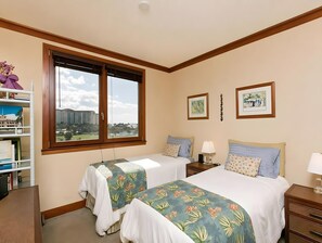 A hotel room with two beds, a window with a city view, a bookshelf, and two framed pictures on the wall. - Ko Olina, Ko Olina Beach Villas, Spacious 6 BR, Beachfront, Sleeps 16 (Kapolei)