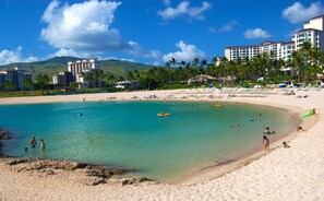 A beach with clear turquoise water, palm trees, and resort buildings in the background. - Ko Olina, Ko Olina Beach Villas, Spacious 6 BR, Beachfront, Sleeps 16 (Kapolei)
