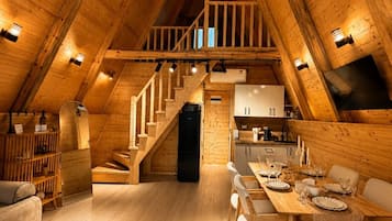 A wooden interior with a dining area, kitchen, and staircase leading to a loft.