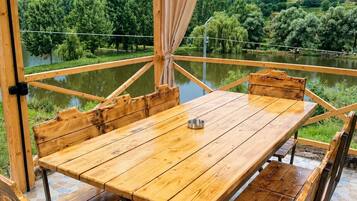 An outdoor wooden table and benches with a view of a lake and hills.