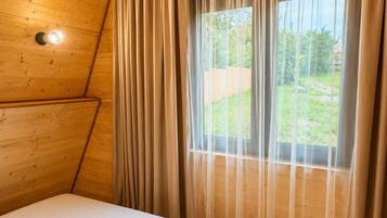 Une chambre avec un plafond en bois, un lit doté d’un matelas blanc et une fenêtre ornée de rideaux légers.