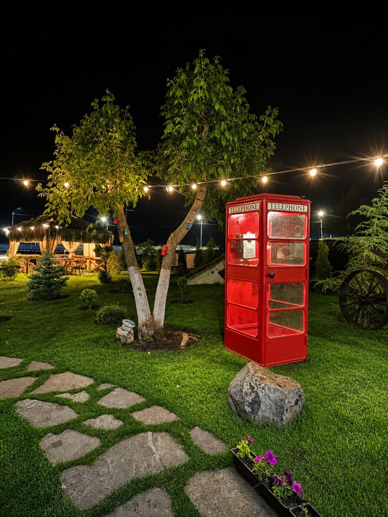 Une cabine téléphonique rouge dans un jardin, la nuit.