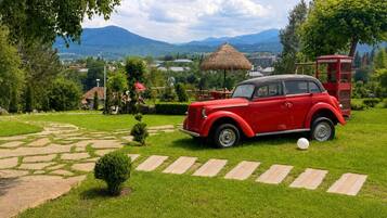 Ein rotes Oldtimer-Auto auf einem gepflasterten Weg in einem üppigen Garten mit Bergblick.