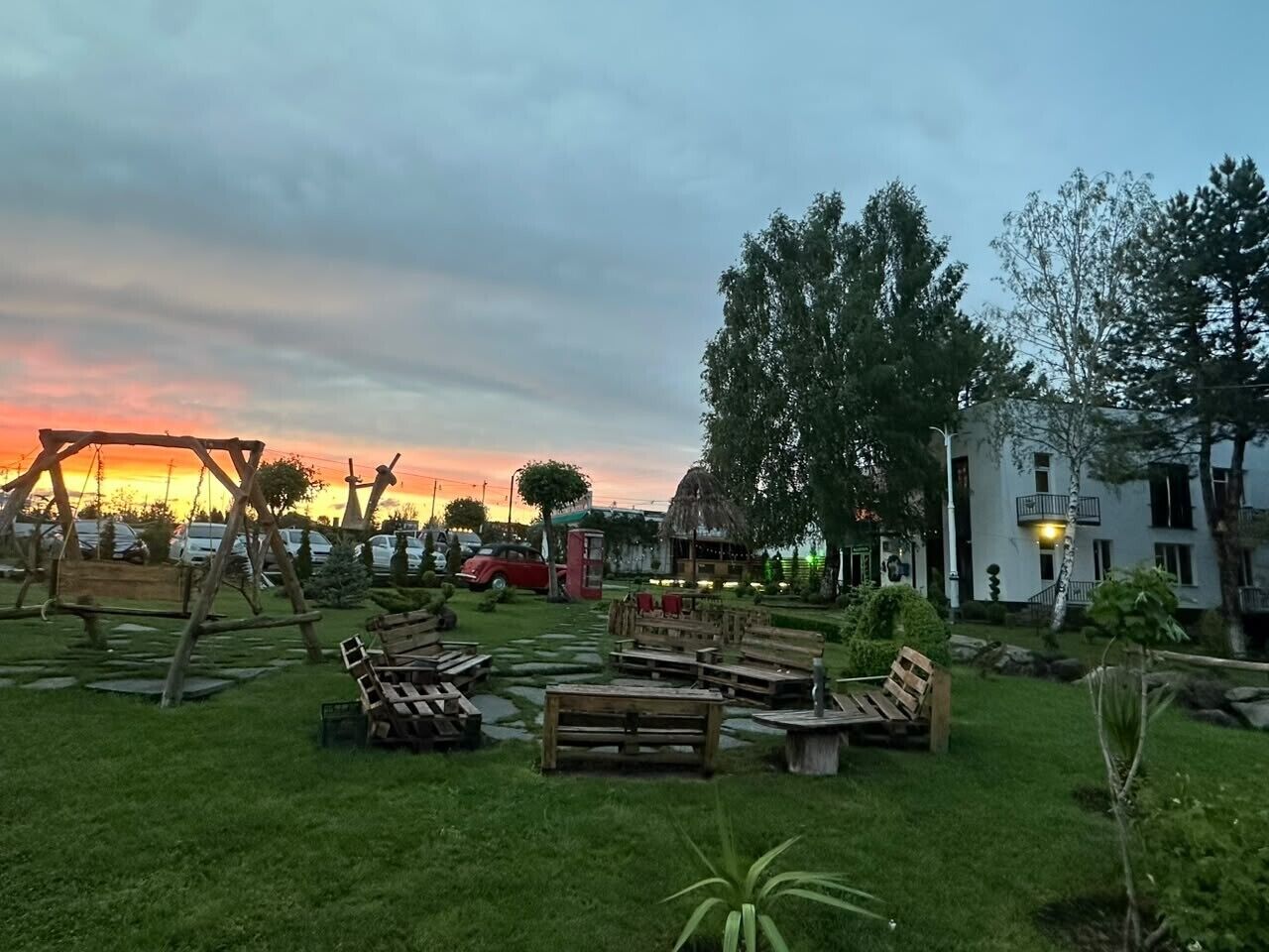 Un espace extérieur aménagé avec des bancs et des tables en bois, entouré de verdure et d’arbres.