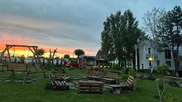 Un espace extérieur aménagé avec des bancs et des tables en bois, entouré de verdure et d’arbres.