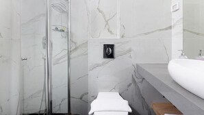 A modern bathroom with a glass shower enclosure, a white sink, and marble walls. - Razin 37 (Eilat)