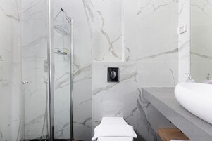 A modern bathroom with a glass shower enclosure, a white sink, and marble walls.