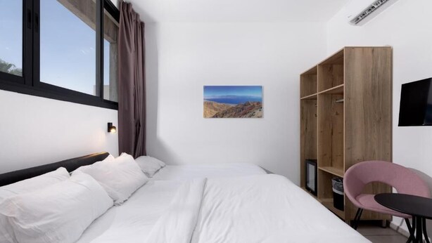A bedroom with a bed, a wooden wardrobe, a desk, a chair, and a wall-mounted TV. - Razin 37 (Eilat)