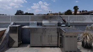 An outdoor kitchen with a built-in grill, sink, and storage cabinets. - Razin 37 (Eilat)
