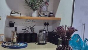 Eine Küchenarbeitsplatte mit Kaffeemaschine, Wasserkocher, einer Vase mit Trockenblumen und einer blauen Tasche.