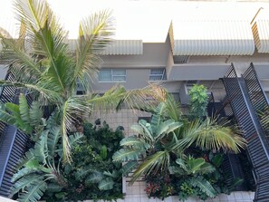 A residential building with a gated entrance, a tiled pathway, and a variety of tropical plants.