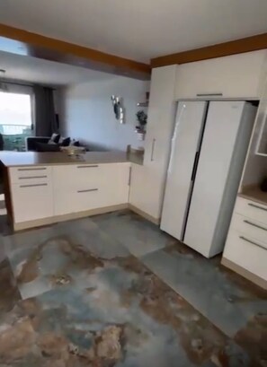 A kitchen with white cabinets, a refrigerator, and a countertop. - Luxurious Beach Apartment (Westbrook)
