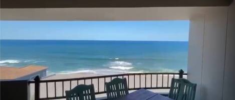 A balcony with a table and chairs overlooking the ocean.