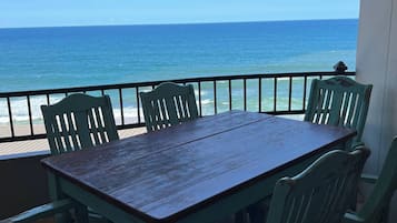 A wooden table with chairs on a balcony overlooking the ocean.