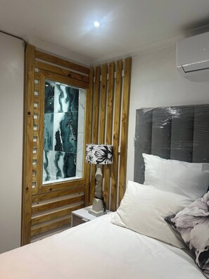 A bedroom with a bed, a nightstand, a lamp, a window with a view, and an air conditioning unit. - Luxurious Beach Apartment (Westbrook)
