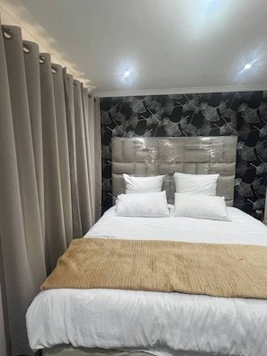 A hotel room with a large bed, a headboard, and a patterned wall. - Luxurious Beach Apartment (Westbrook)