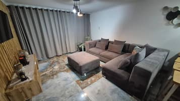 A living room with a sectional sofa, a wooden sideboard, and a patterned rug.